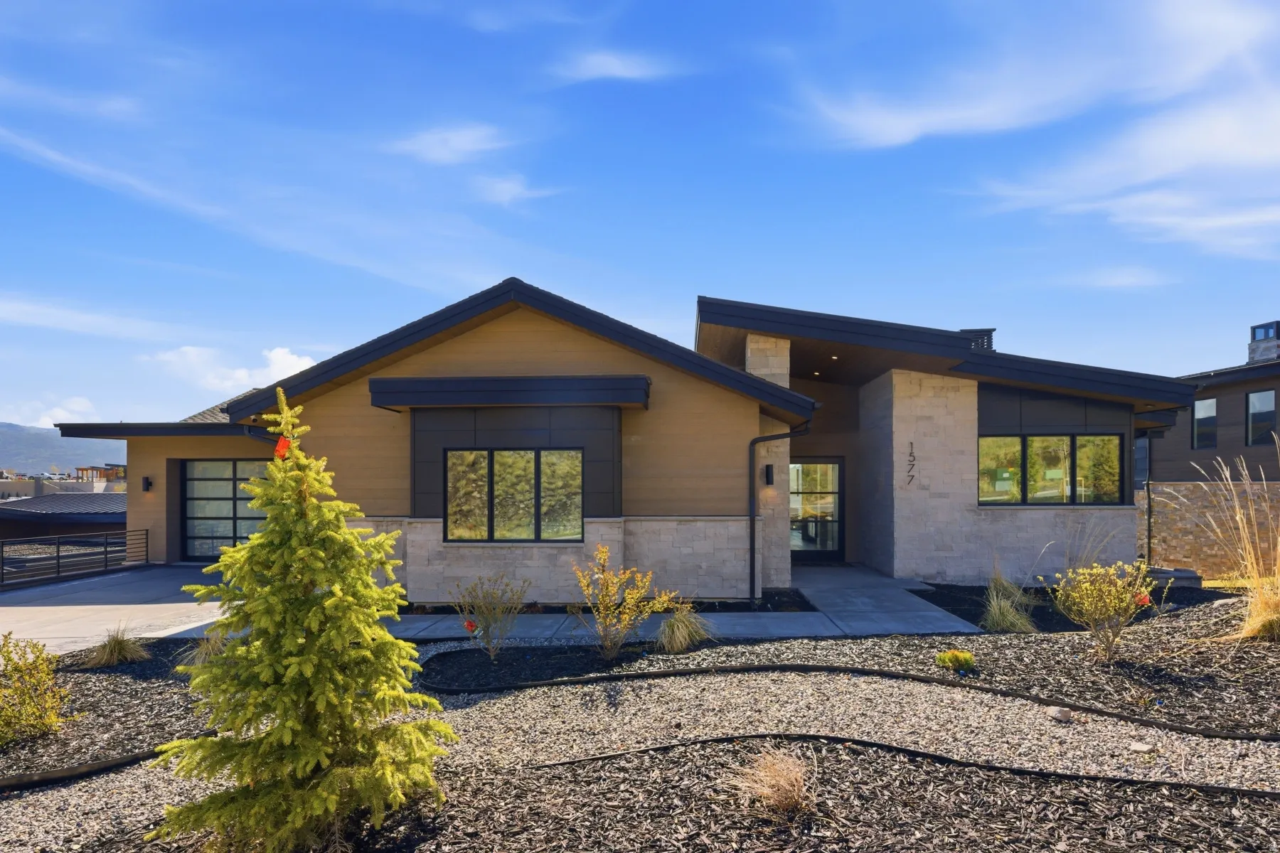 Modern home featuring a garage, driveway, and stone siding