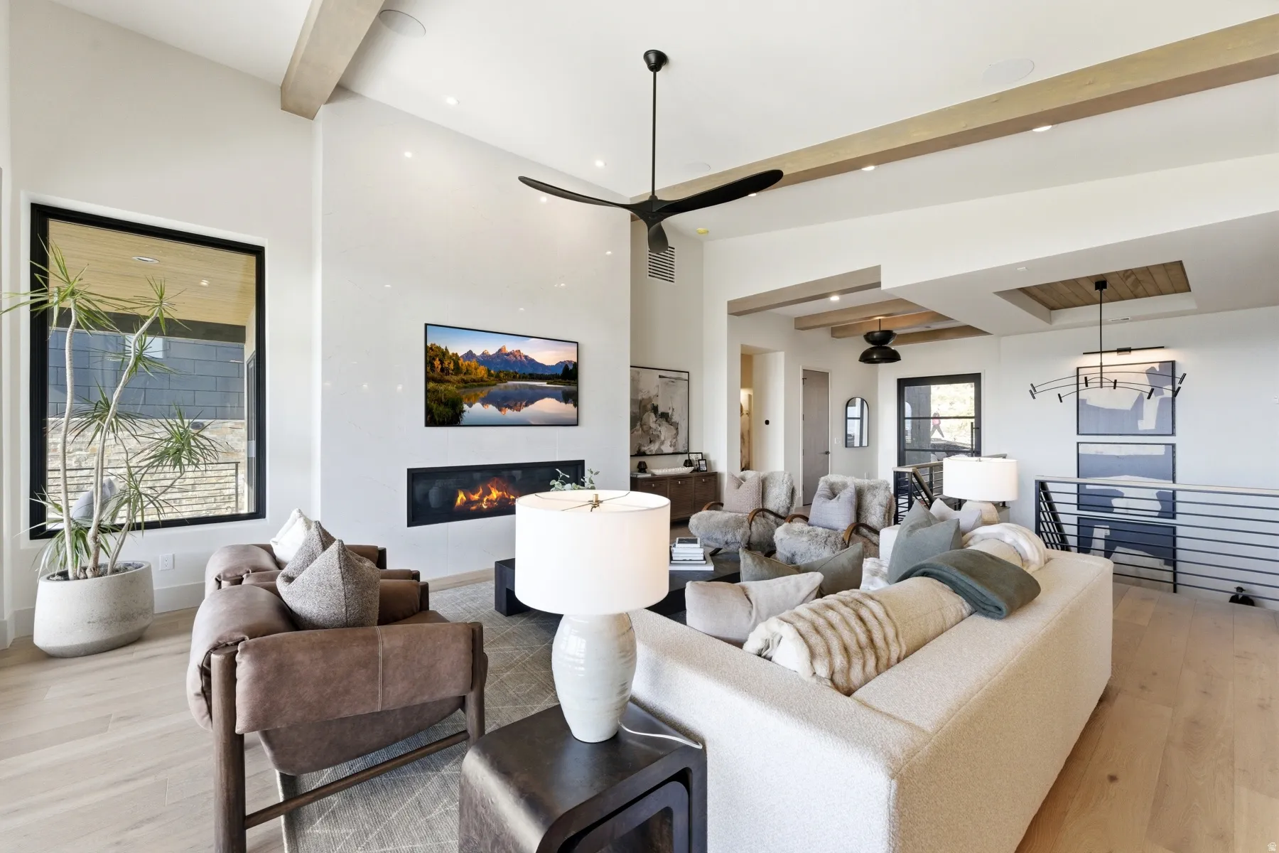 Living area with light wood finished floors, a glass covered fireplace, hanging lights, and vaulted ceiling with beams