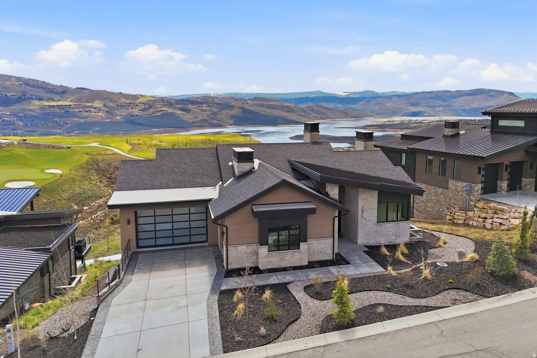 Modern home featuring stone siding, a chimney, concrete driveway, a water and mountain view, and a garage