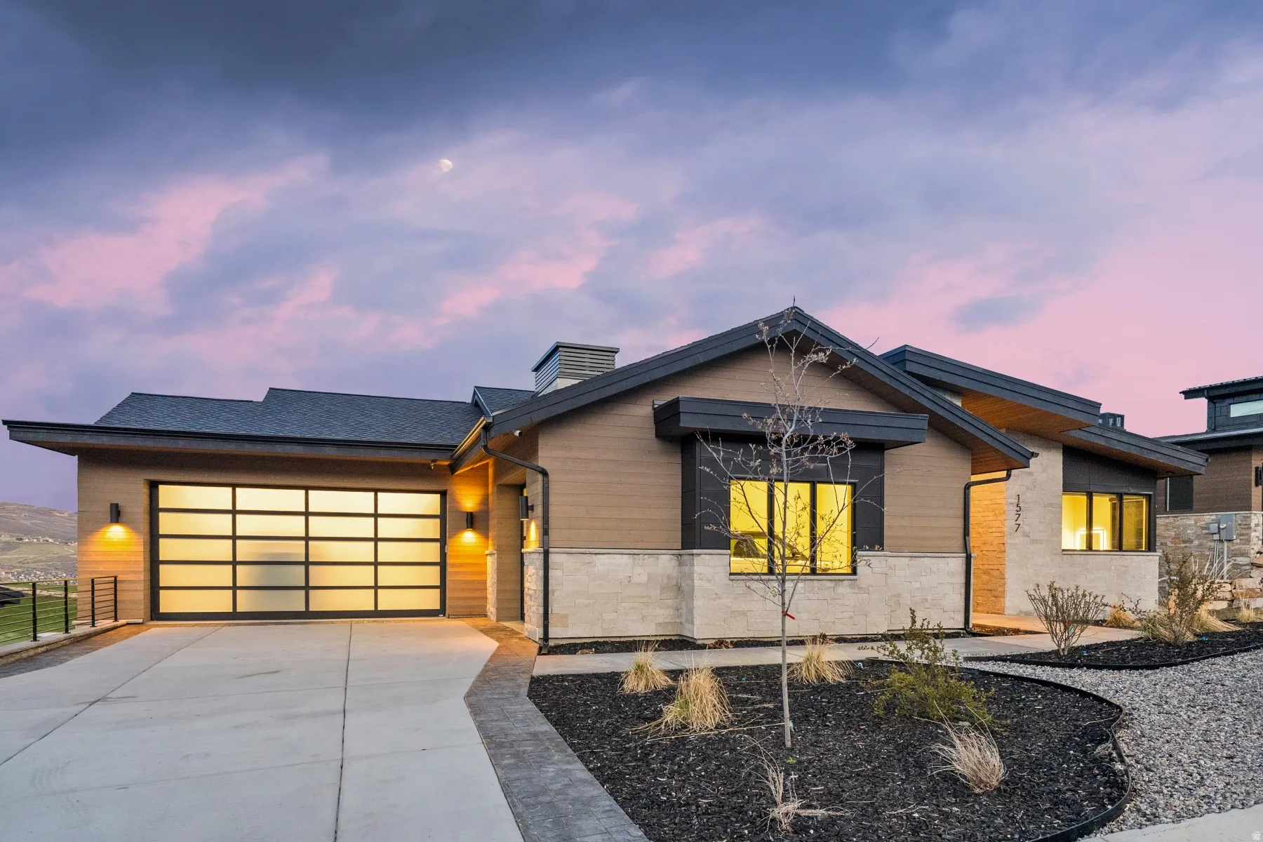 Modern home with a garage, concrete driveway, stone siding, and a chimney