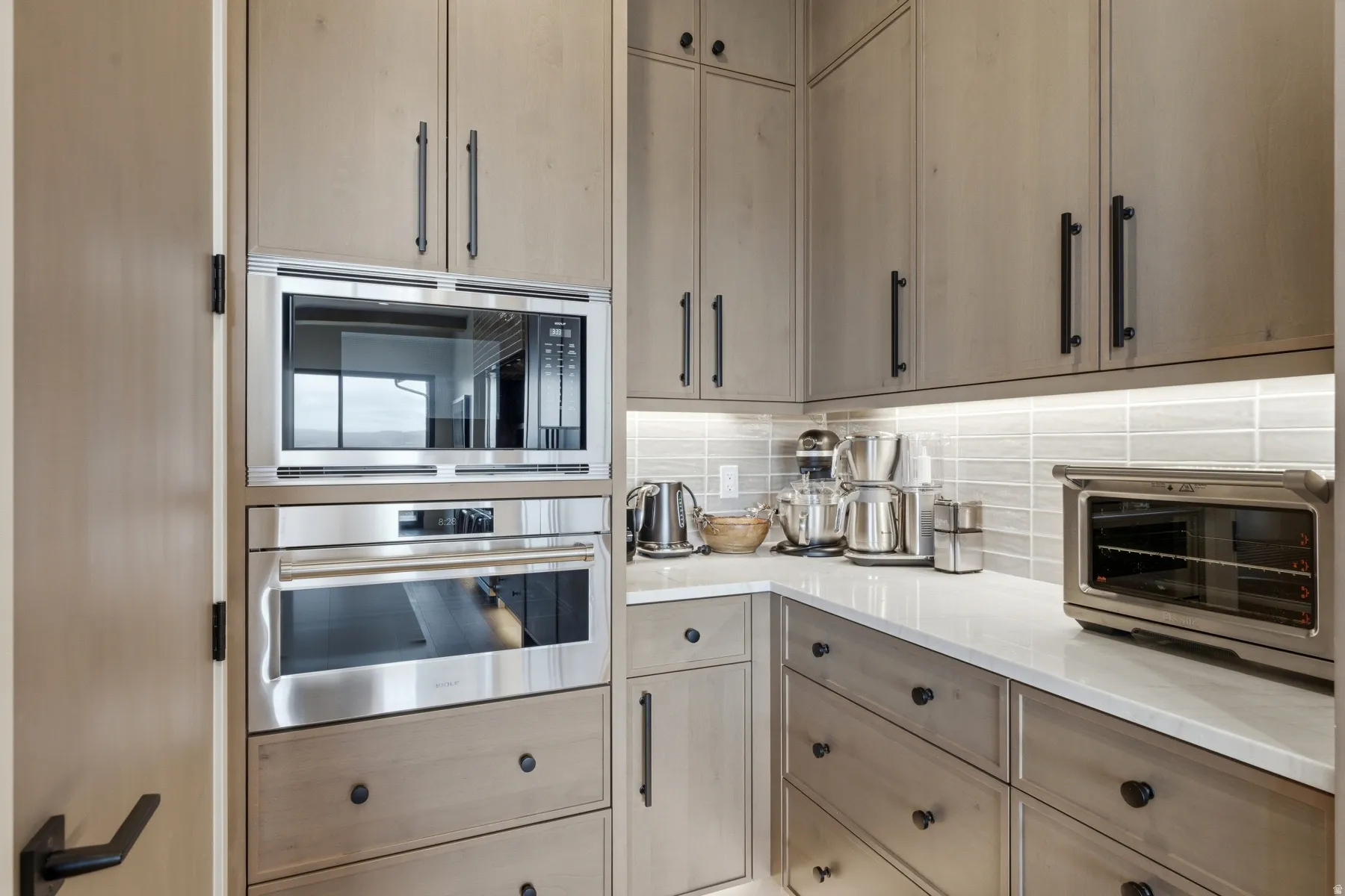 Kitchen featuring stainless steel appliances, decorative backsplash, light wood finish cabinets, and light stone counters