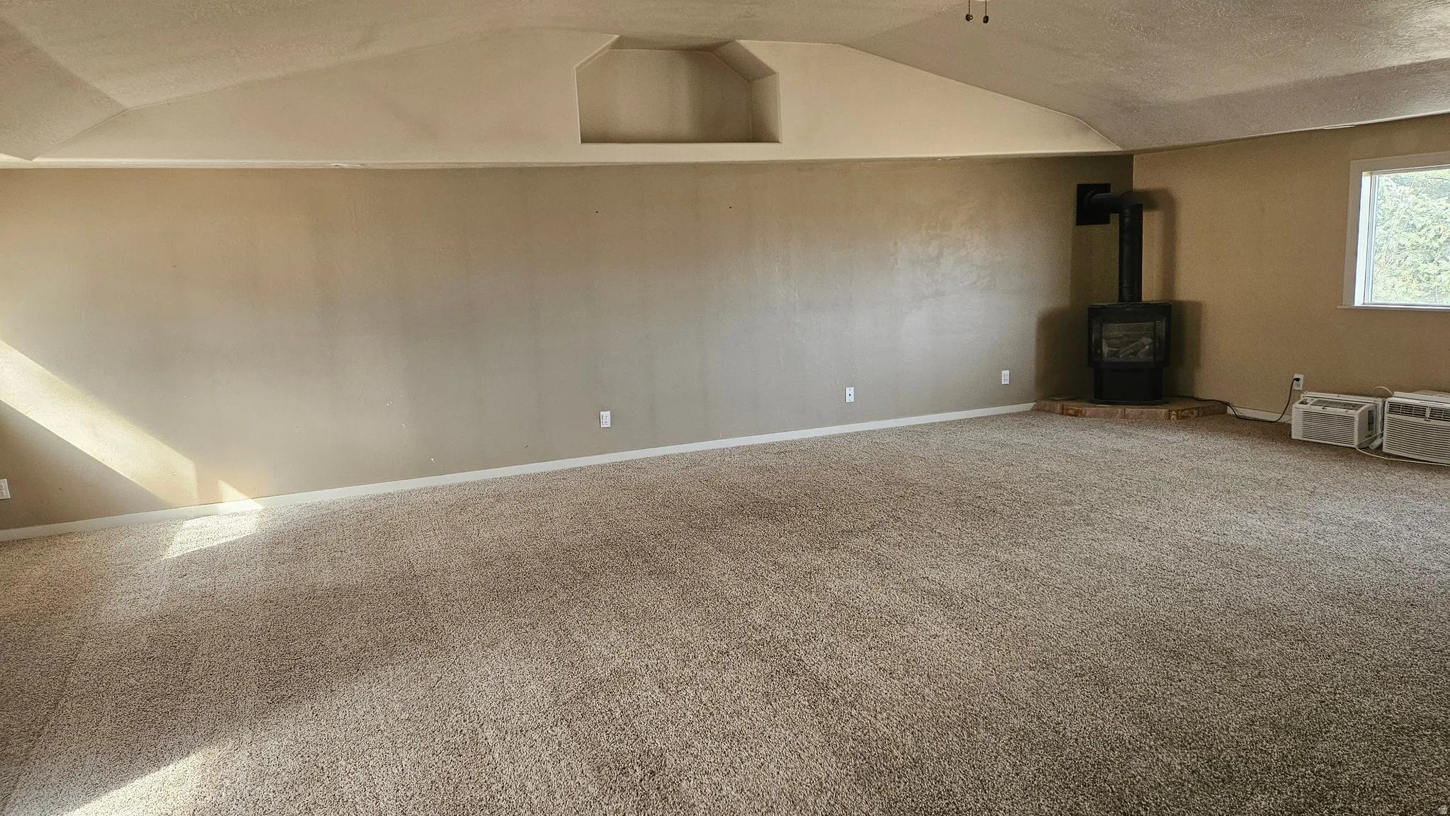 Unfurnished living room with carpet flooring, a wood stove, and a textured ceiling