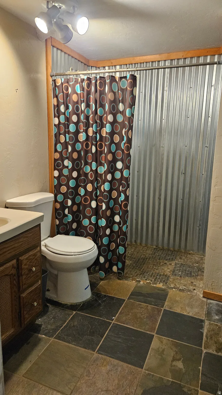 Full bath featuring vanity, stone tile flooring, and curtained shower