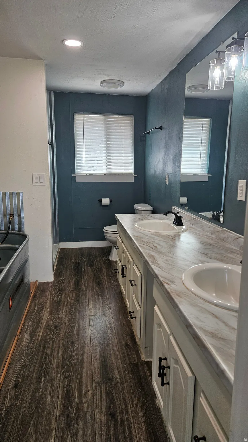 Full bathroom featuring double vanity, dark wood-style floors, plenty of natural light, and a garden tub