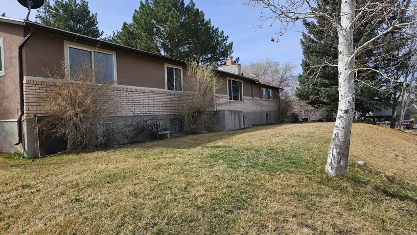 View of side of home featuring brick siding, a chimney, stucco siding, and a lawn