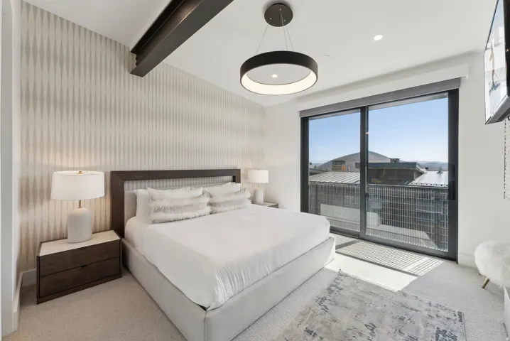 Bedroom featuring wallpapered walls, light colored carpet, beam ceiling, access to exterior, and an accent wall