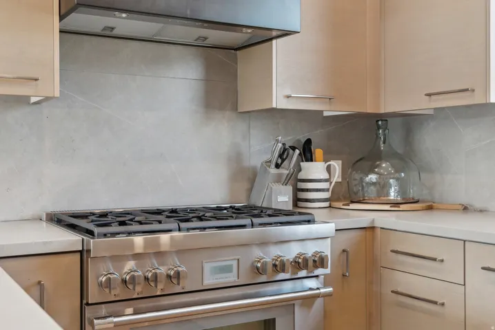 Kitchen with extractor fan, high end stainless steel range, decorative backsplash, and light wood finish cabinets