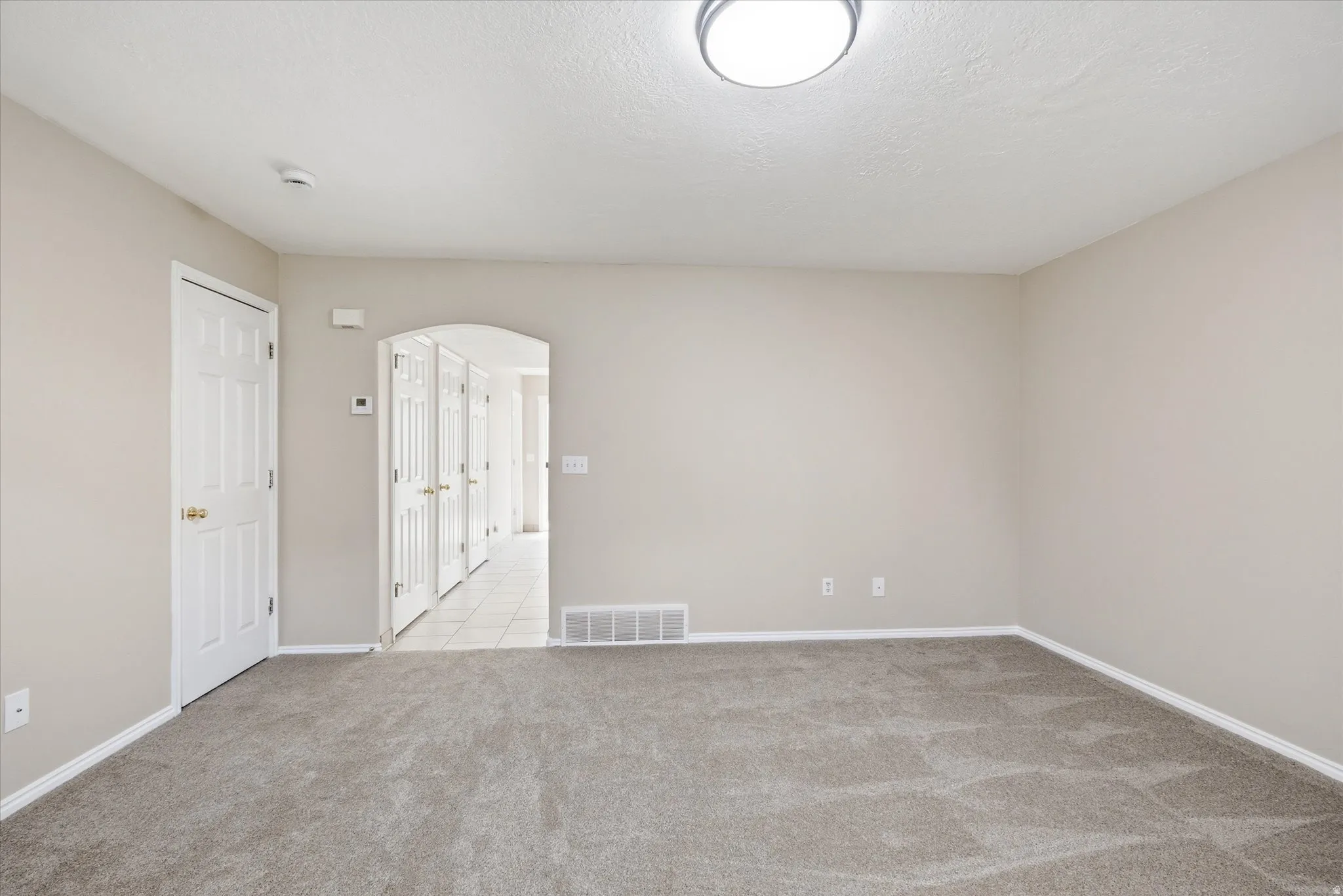 Spacious room featuring neutral carpeting, light neutral wall paint, and white baseboards