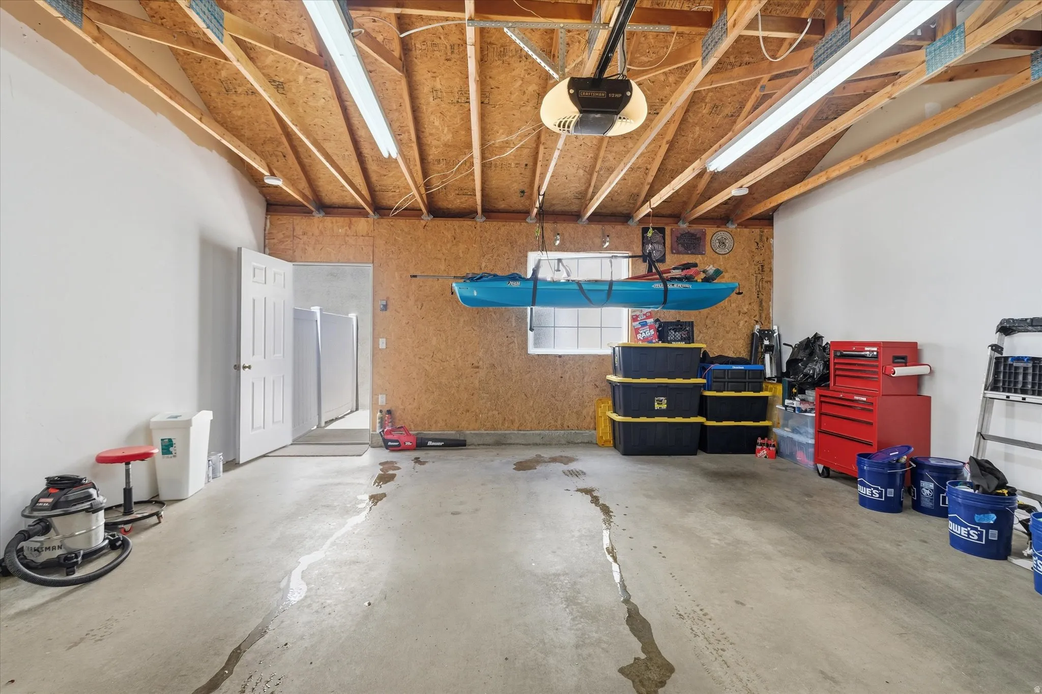 Spacious garage featuring a concrete floor, exposed wood ceiling beams, and overhead fluorescent lighting