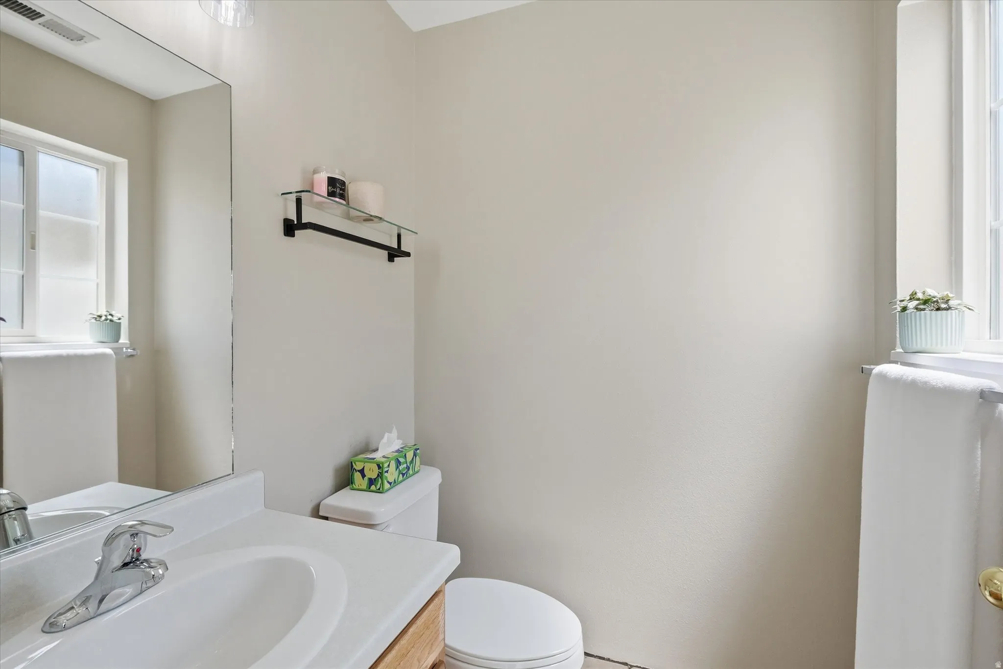 Bathroom featuring a vanity with a white countertop and integrated sink, a chrome faucet, a large wall-mounted mirror, a toilet, and a window with natural light
