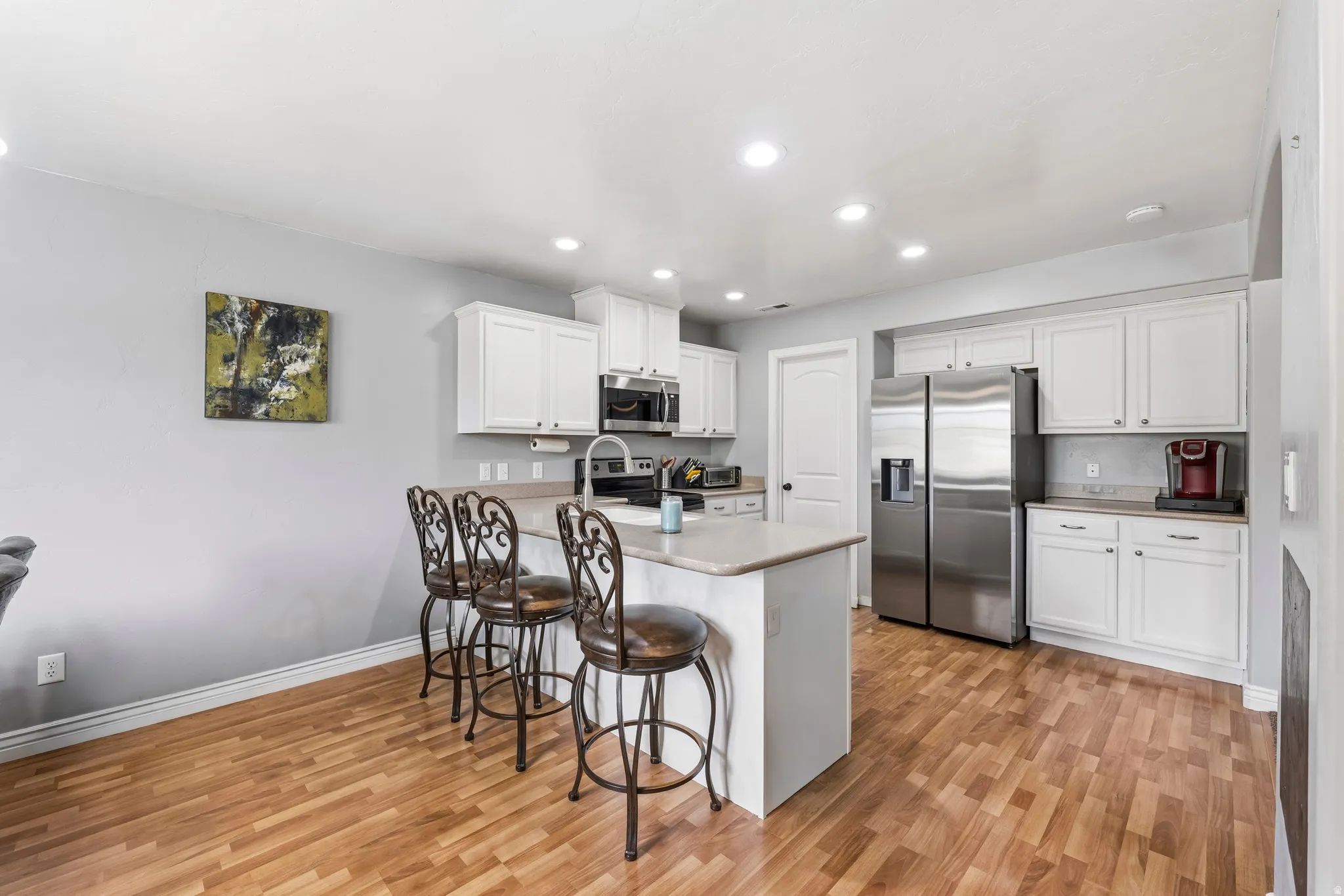Kitchen featuring stainless steel appliances, white cabinetry, light countertops, a breakfast bar area, and light wood-style flooring