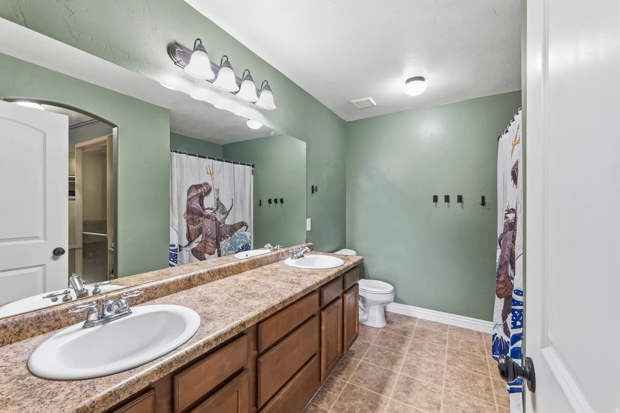Full bathroom with double vanity, curtained shower, and light tile patterned flooring
