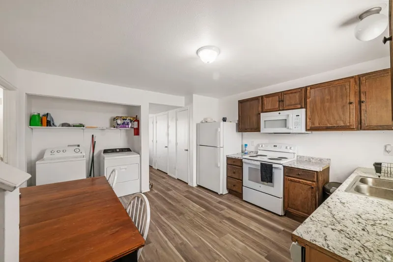 Kitchen featuring white appliances, light countertops, dark wood finished floors, washing machine and clothes dryer, and wood finish cabinetry