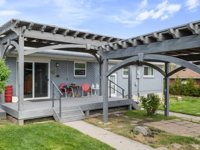 Back of property with a lawn, a wooden deck, brick siding, and a pergola