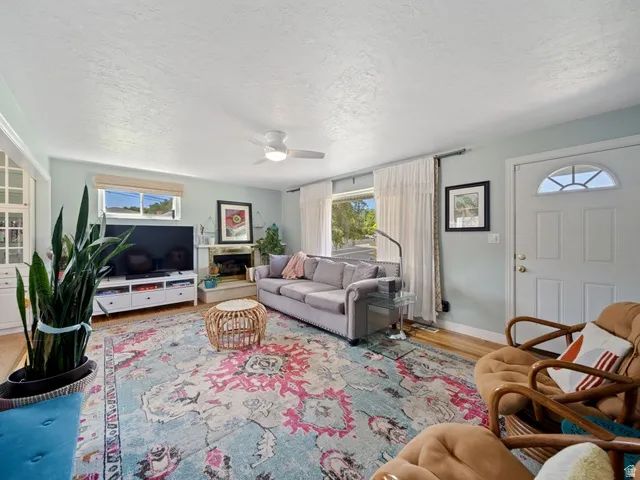 Living area with a textured ceiling, light hard wood flooring, gas fireplace and ceiling fan