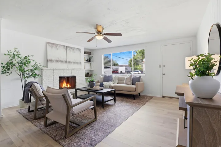 Living area with light wood-style flooring, ceiling fan, and a brick fireplace
