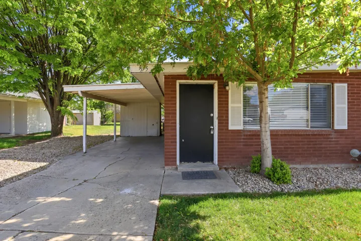 Entrance to property featuring a lawn, an attached carport, concrete driveway, and brick siding