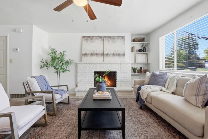 Living area featuring a ceiling fan, dark wood-style floors, and a brick fireplace