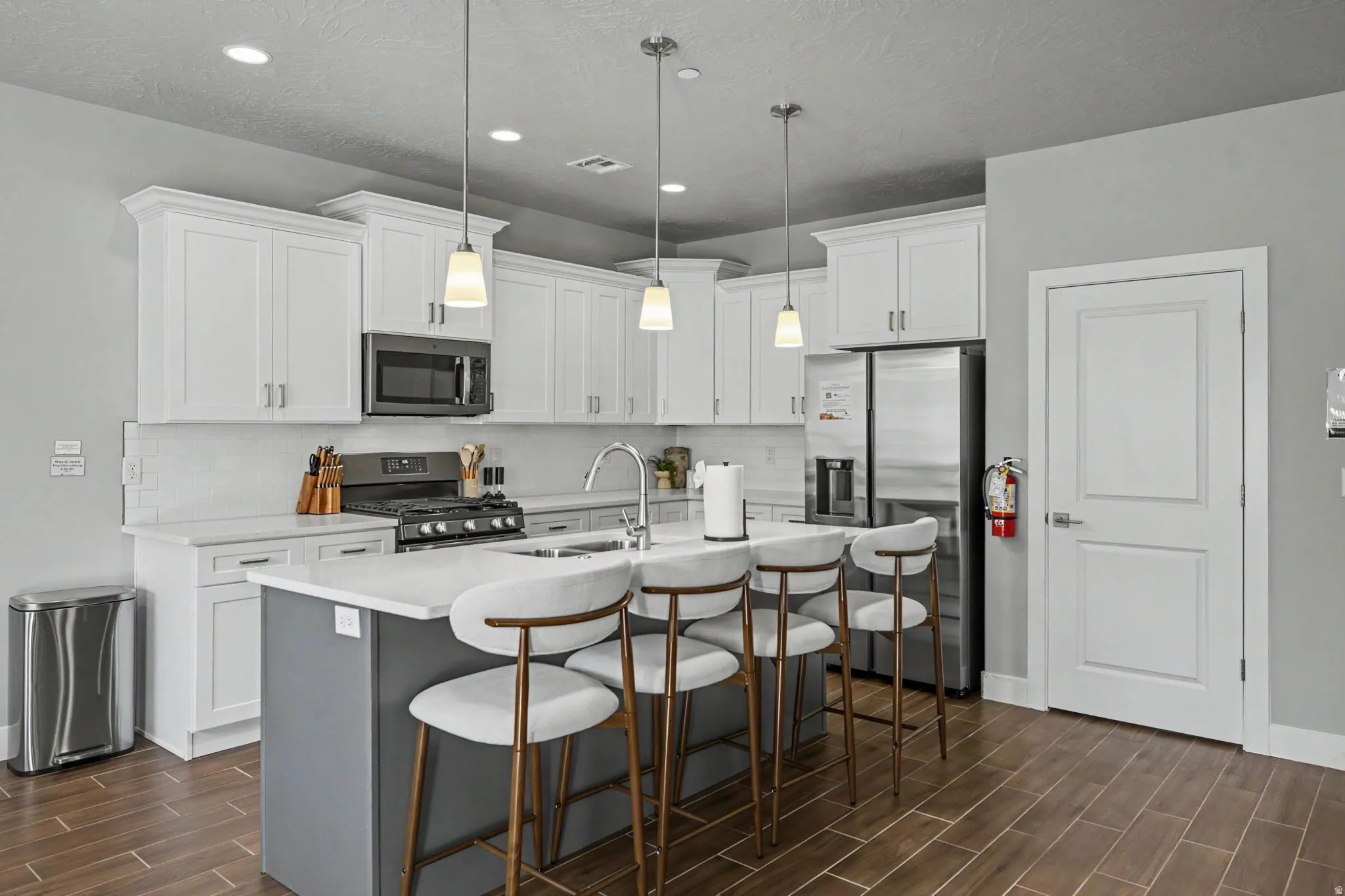 Kitchen featuring white cabinetry, stainless steel appliances, a center island with pendant lighting, and wood-finish flooring