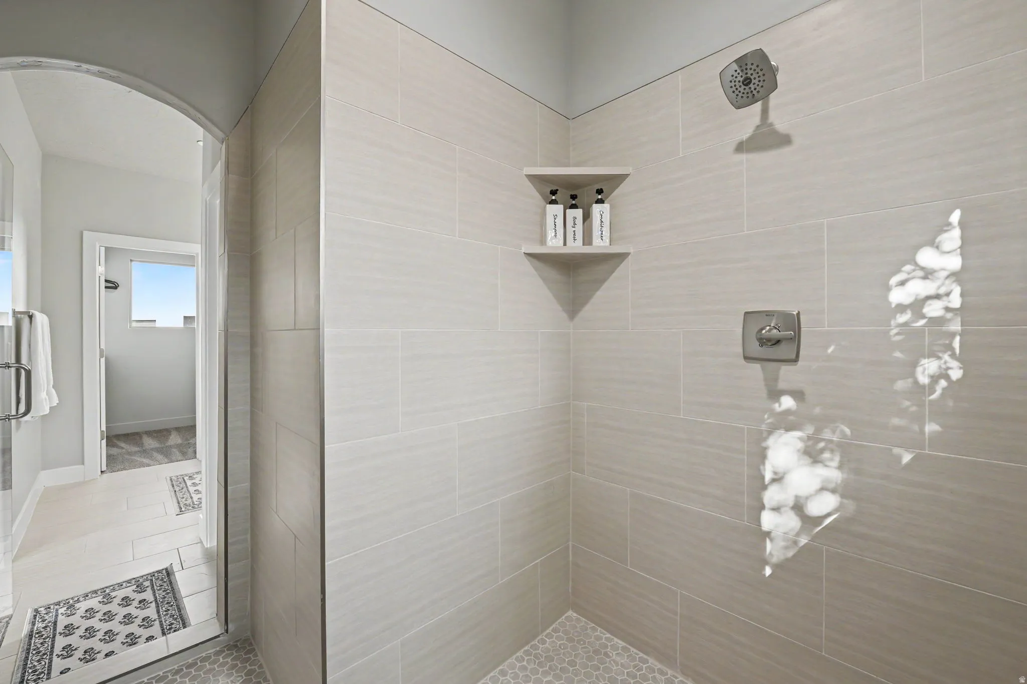 Walk-in shower with light-toned rectangular wall tiling, hexagonal floor tiling, and built-in corner shelving