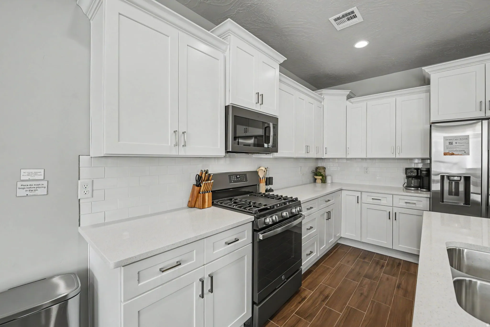 Modern kitchen featuring white cabinetry, light-toned countertops, a white subway tile backsplash, and wood-finish flooring