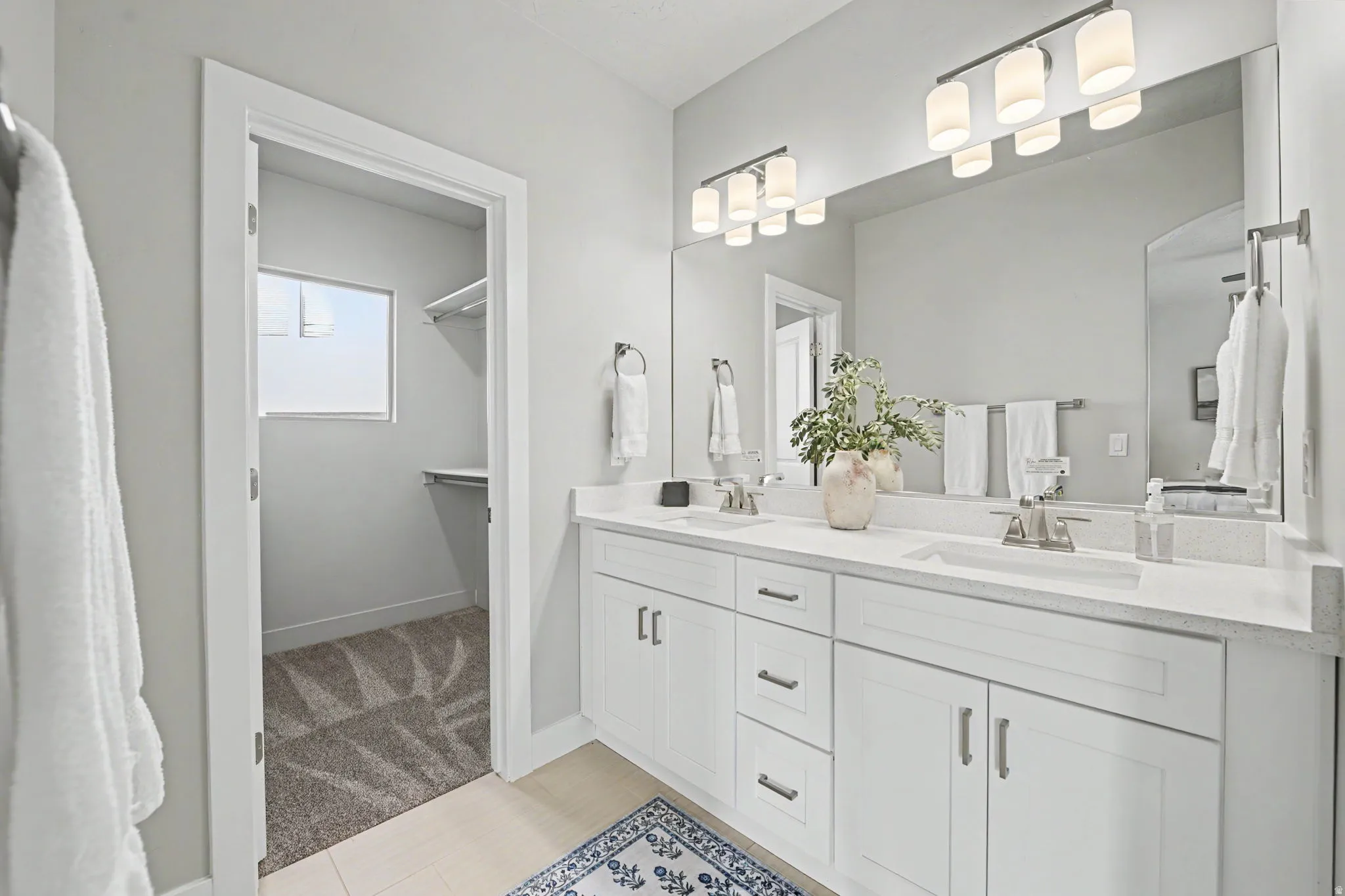Double vanity with under-sink cabinetry and drawers, quartz countertops, dual framed mirrors, and a walk-in closet with built-in shelving