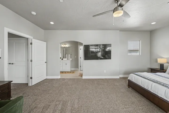 Spacious room featuring neutral carpeting, a ceiling fan with integrated lighting, recessed lighting, and a broad arched doorway
