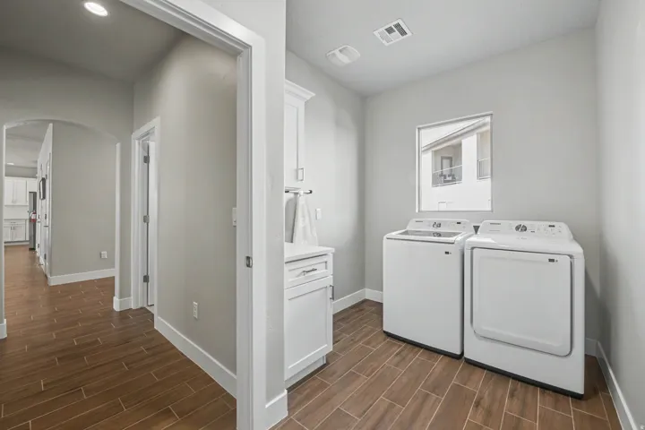 Dedicated laundry area featuring wood-finish flooring, a window, built-in white cabinetry, and a countertop space