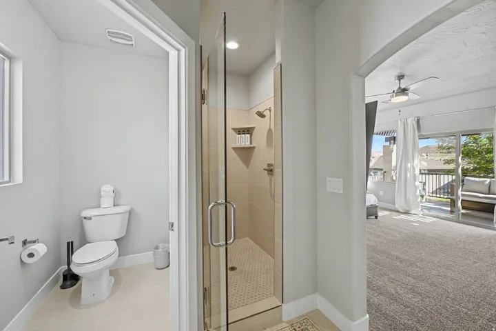 Glass-enclosed shower with tile surround and integrated shelving, featuring a separate toilet area with window