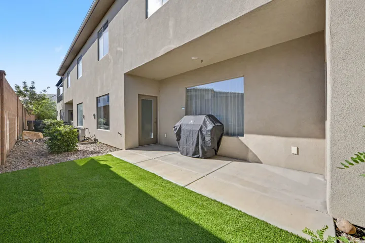 Expansive rear patio with concrete hardscaping adjoins a manicured lawn featuring synthetic turf