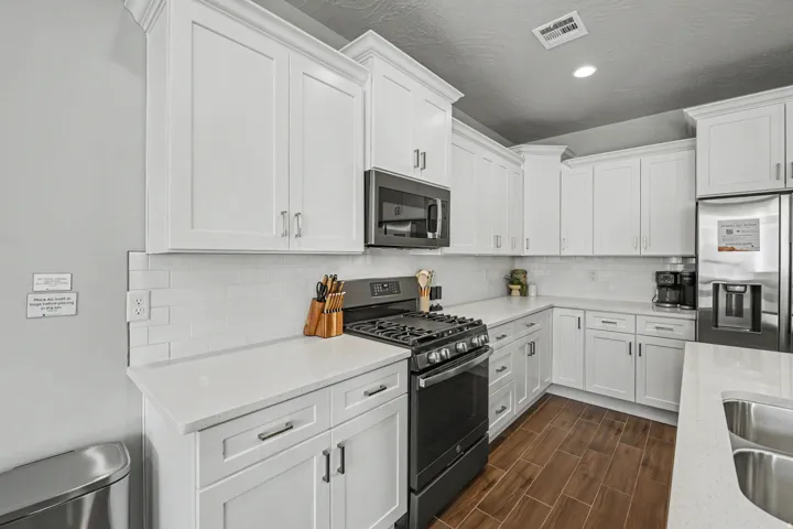 Modern kitchen featuring white cabinetry, light-toned countertops, a white subway tile backsplash, and wood-finish flooring