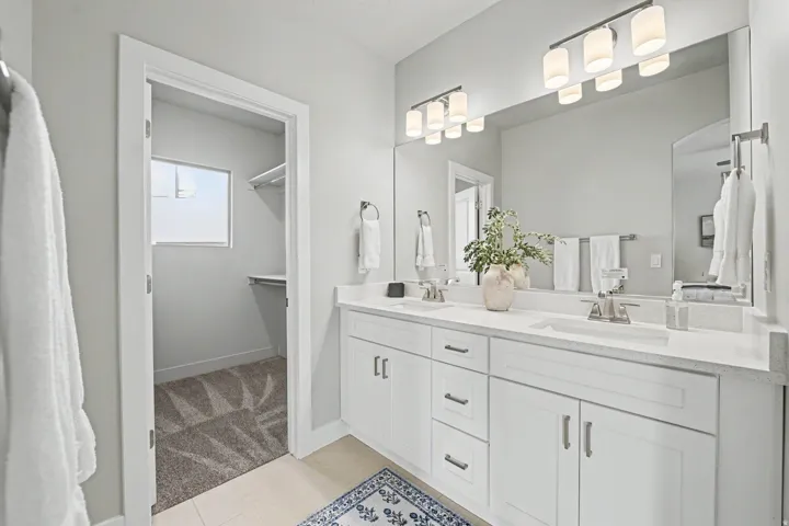 Double vanity with under-sink cabinetry and drawers, quartz countertops, dual framed mirrors, and a walk-in closet with built-in shelving