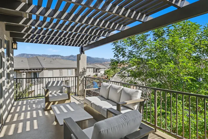 Balcony with a slatted pergola, decorative metal railing, and wall-mounted exterior lighting