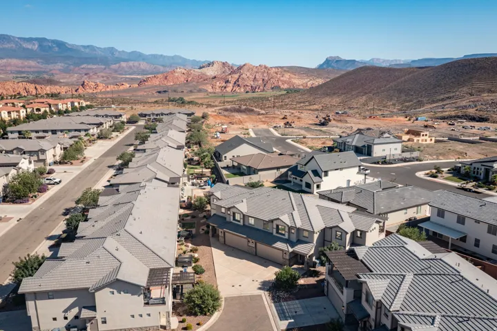 Residential street lined with multi-story homes featuring light-toned exteriors and dark gray roofs, set against a backdrop of arid mountains