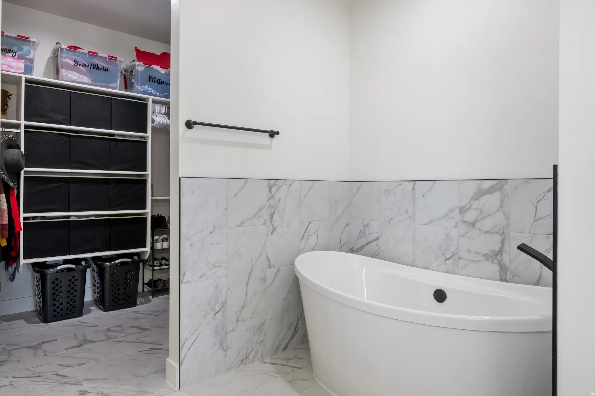 Full bath with light marble finish floors, a freestanding bath, tile walls, and wainscoting