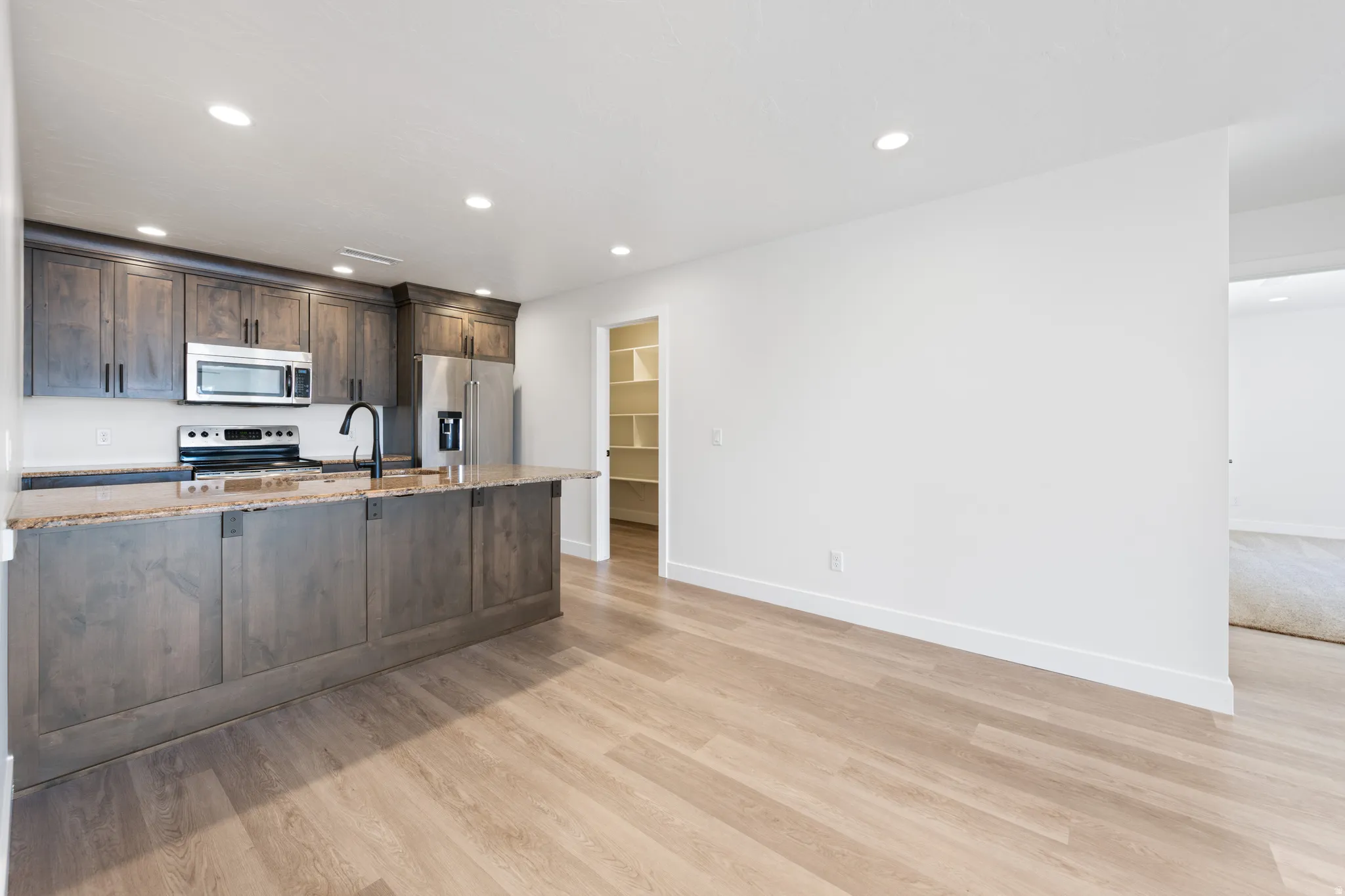 Kitchen with dark wood finish cabinetry, light stone counters, recessed lighting, stainless steel appliances, and light wood-style floors