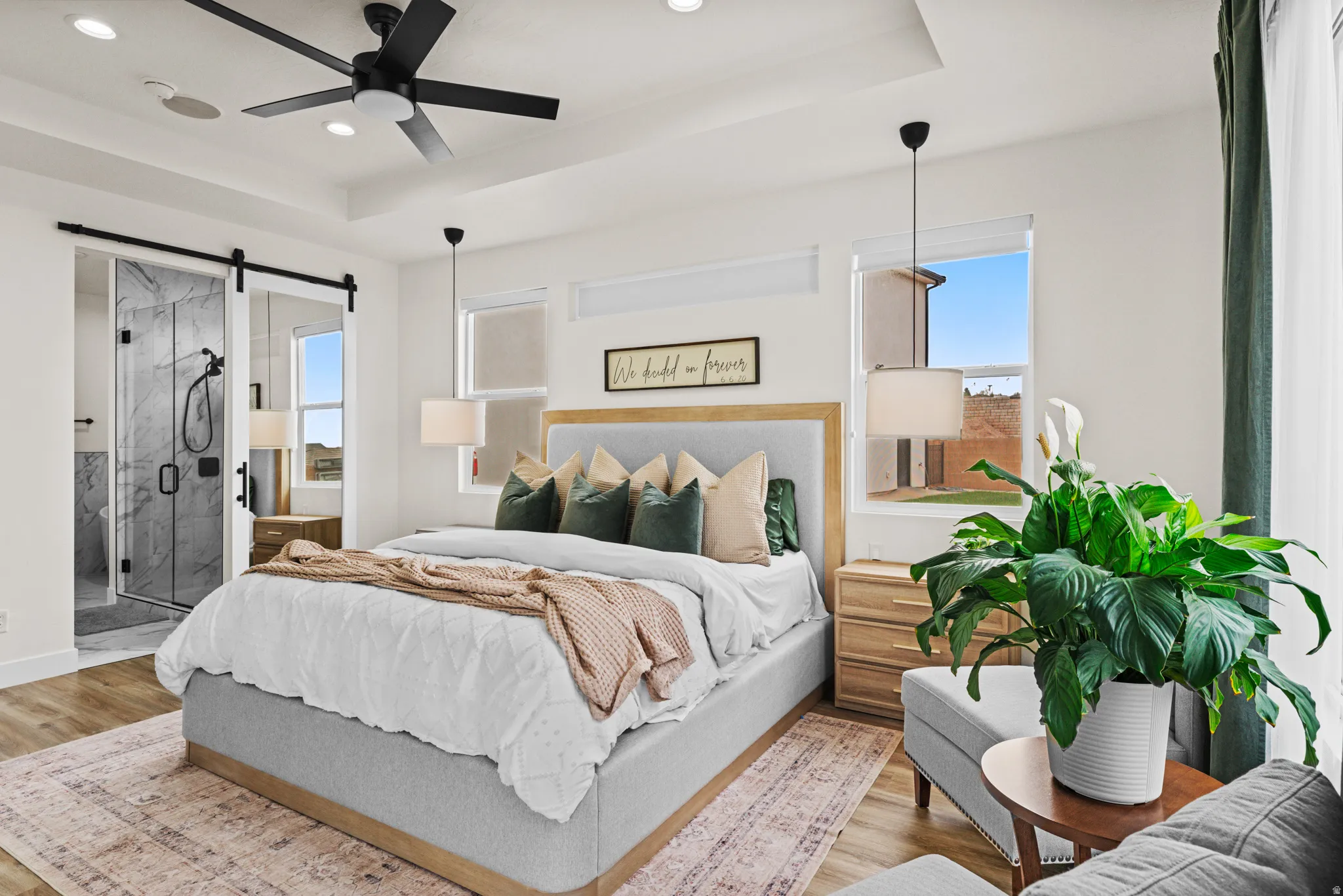 Bedroom with a barn door, a tray ceiling, wood finished floors, a ceiling fan, and ensuite bathroom