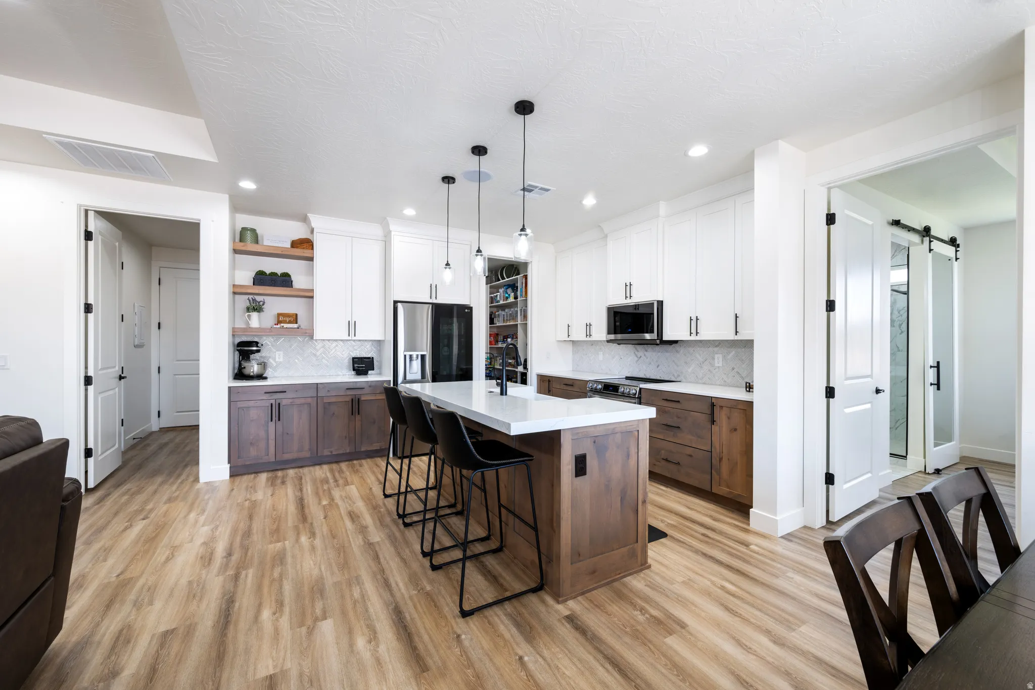 Kitchen with two tone cabinetry, a barn door, stainless steel appliances, a kitchen breakfast bar, and a kitchen island