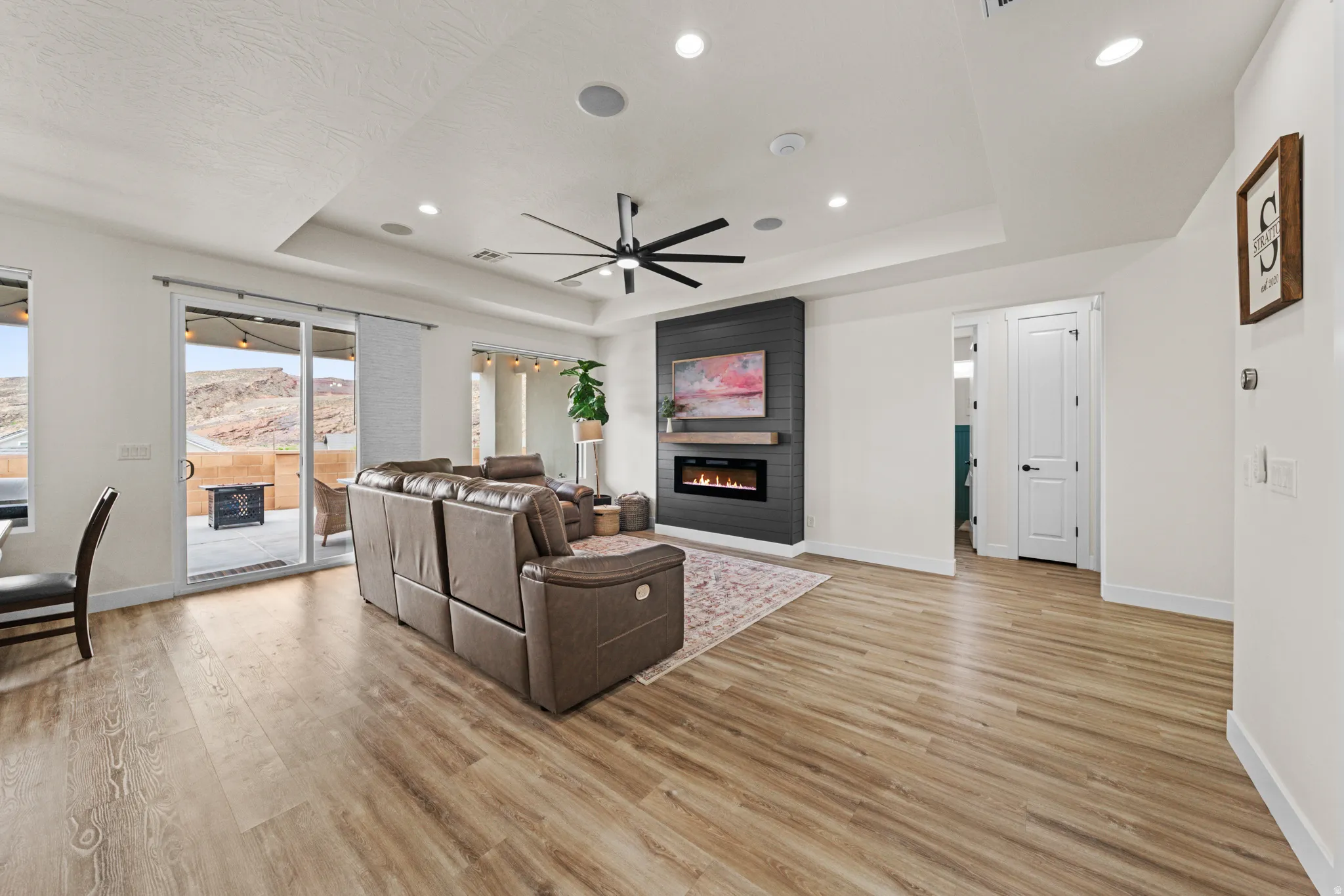 Living area featuring a ceiling fan, light wood-style flooring, a fireplace, recessed lighting, and a tray ceiling