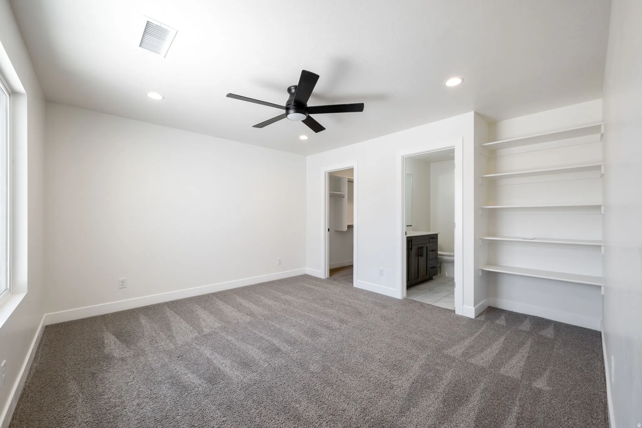 Unfurnished bedroom featuring a spacious closet, light colored carpet, ceiling fan, connected bathroom, and recessed lighting