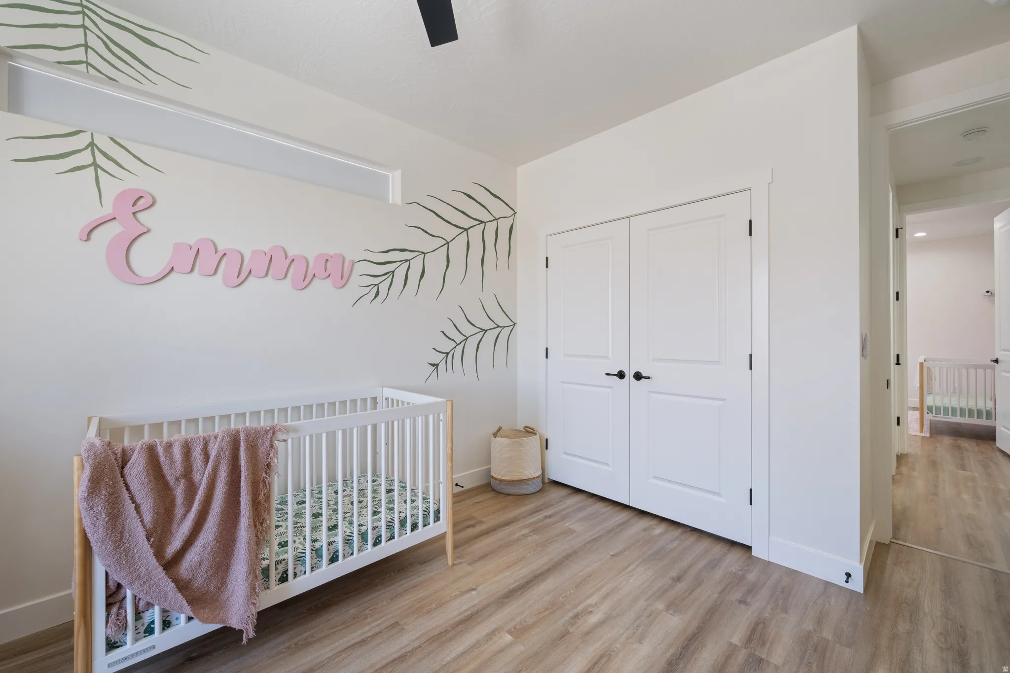 Bedroom featuring a nursery area, light wood-style flooring, a closet, and a ceiling fan