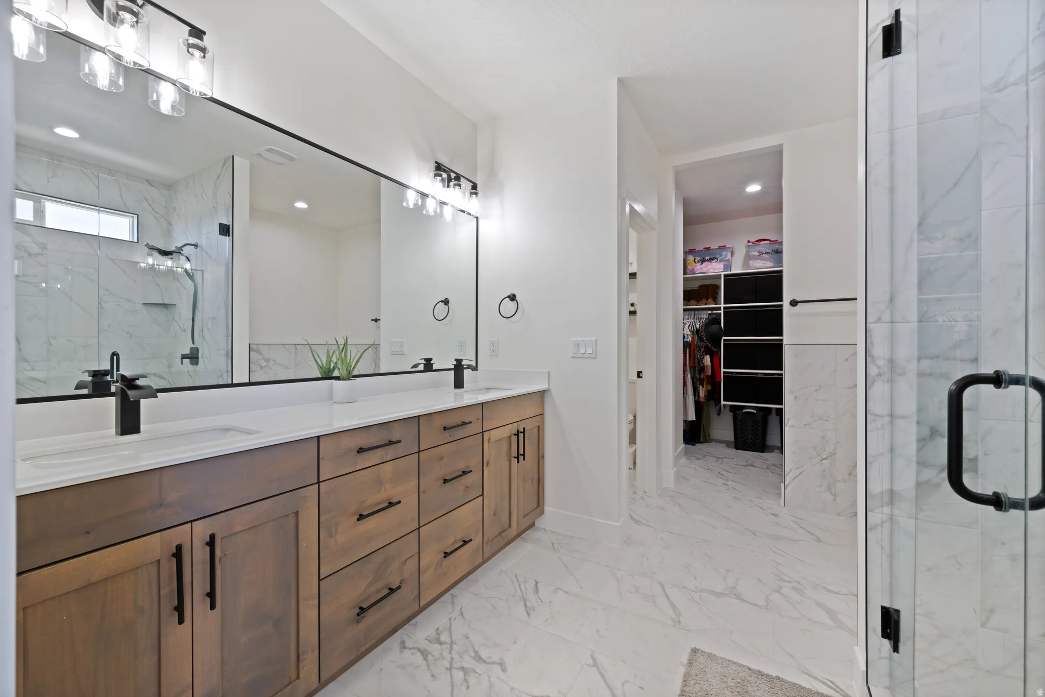 Bathroom with a marble finish shower, double vanity, a spacious closet, and light marble finish flooring