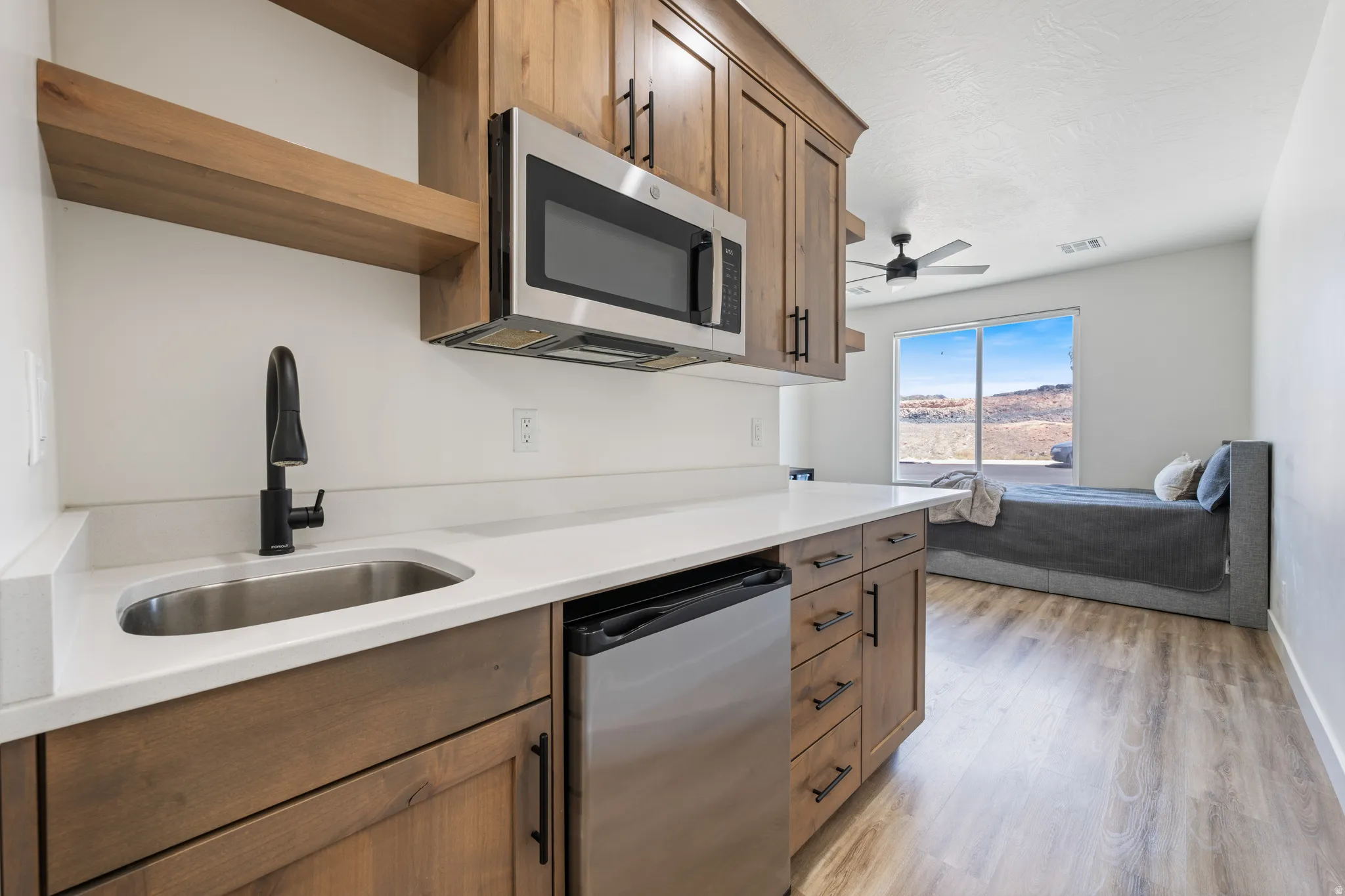 Kitchen with stainless steel appliances, light wood-type flooring, open shelves, wood finish cabinetry, and light stone counters
