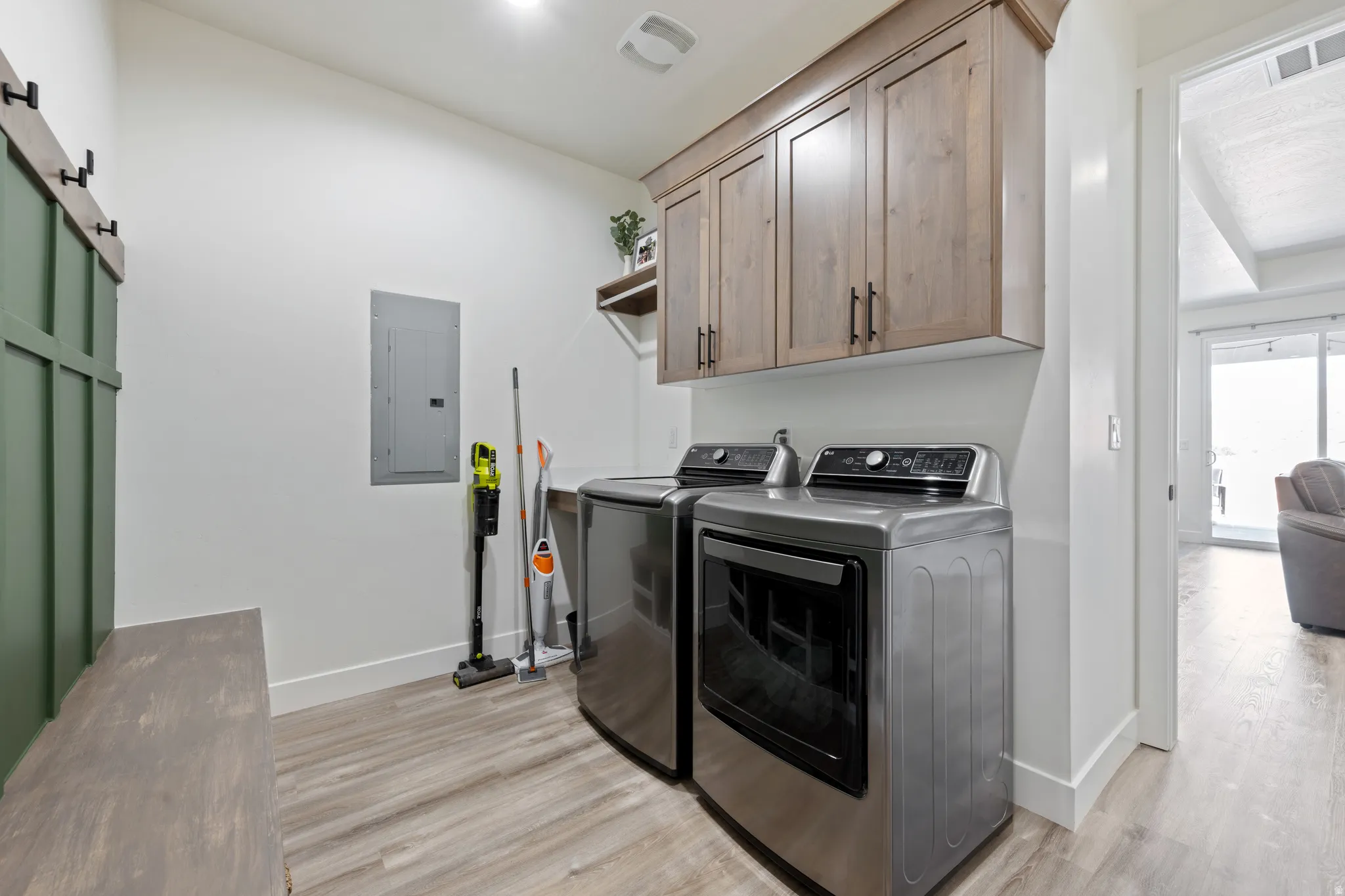 Laundry room with electric panel, light wood-style flooring, a barn door, and cabinet space