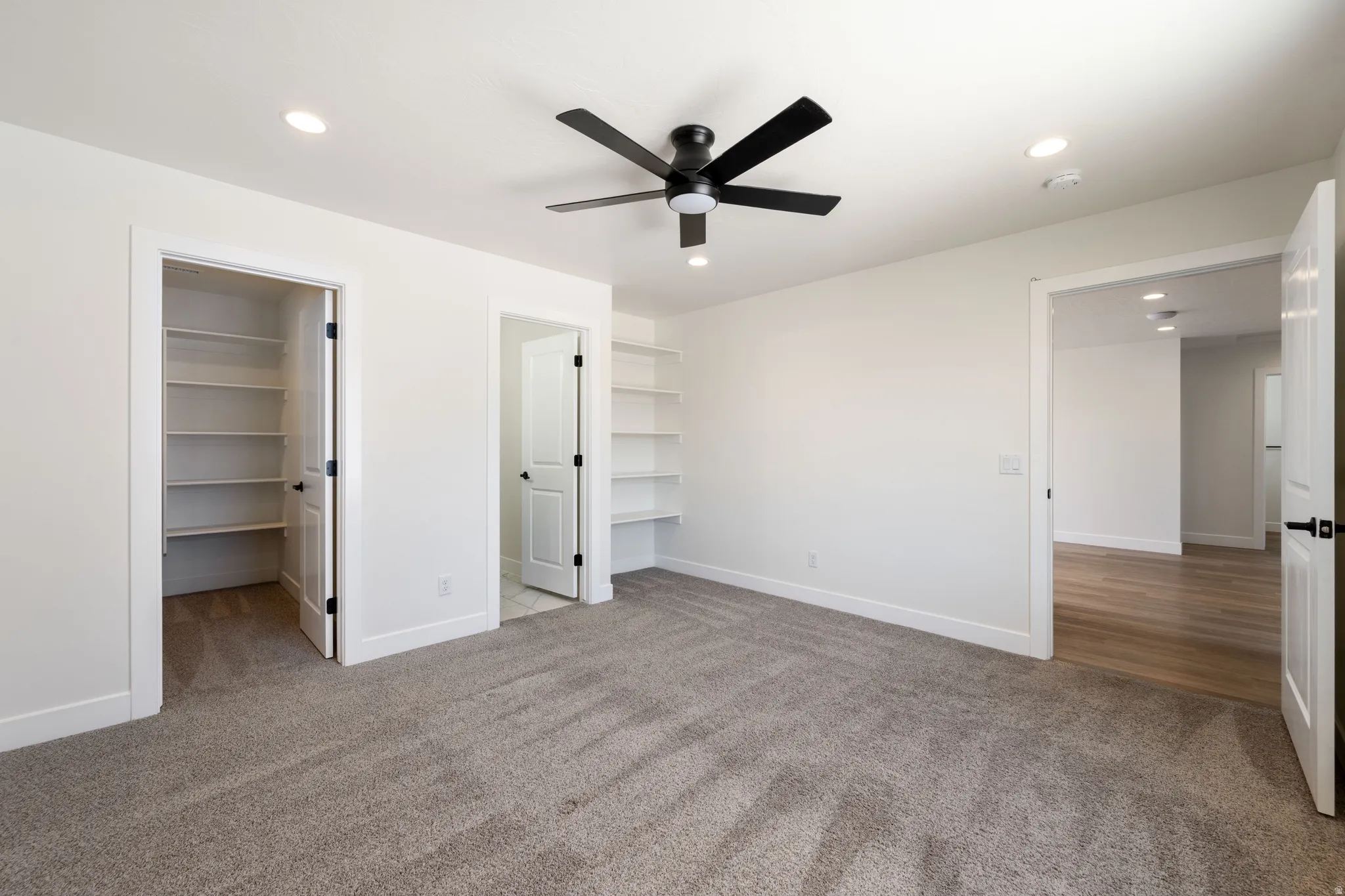 Unfurnished bedroom featuring a walk in closet, light colored carpet, recessed lighting, and a ceiling fan