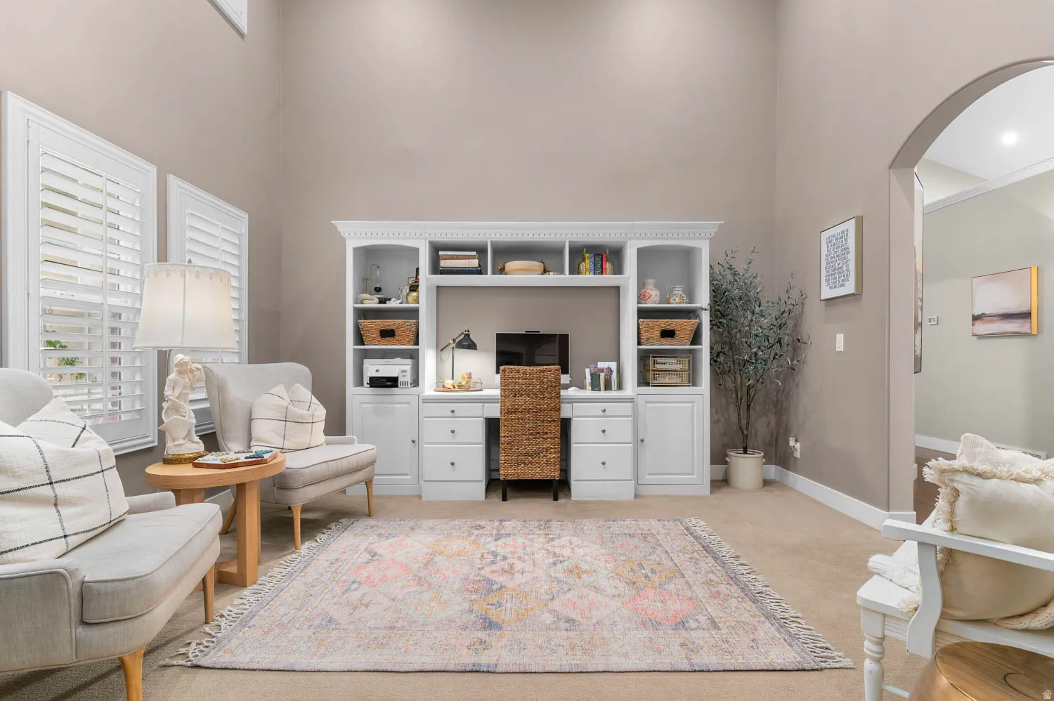 Home office featuring arched walkways, a high ceiling, and light colored carpet