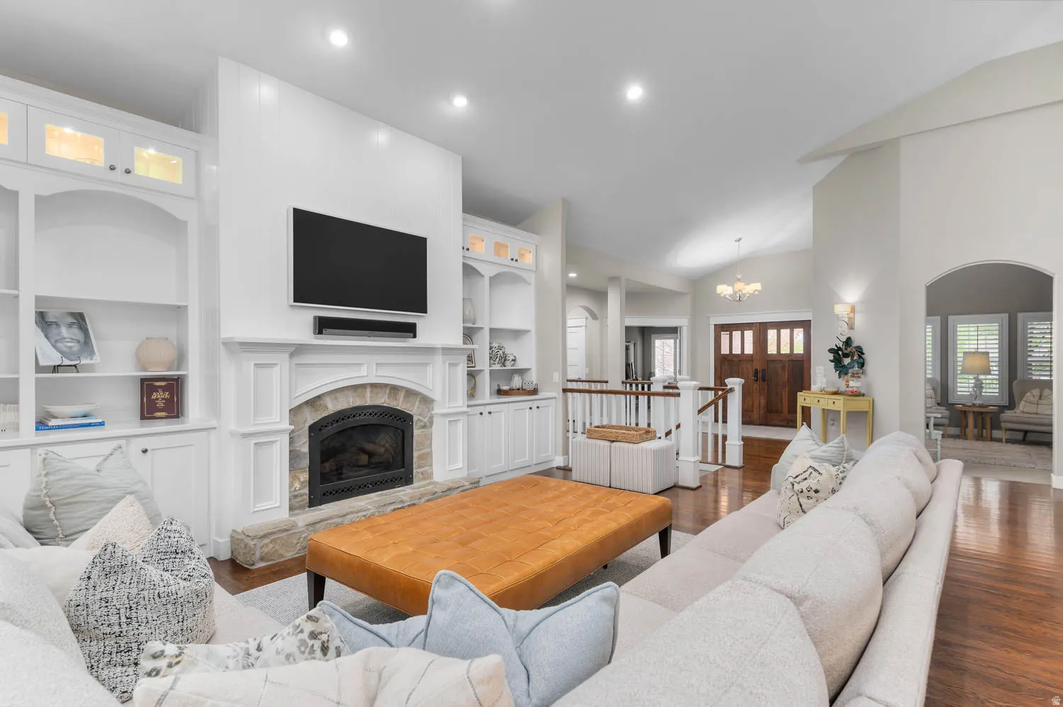 Living area featuring a stone fireplace, lofted ceiling, built in features, dark wood-style flooring, and a chandelier