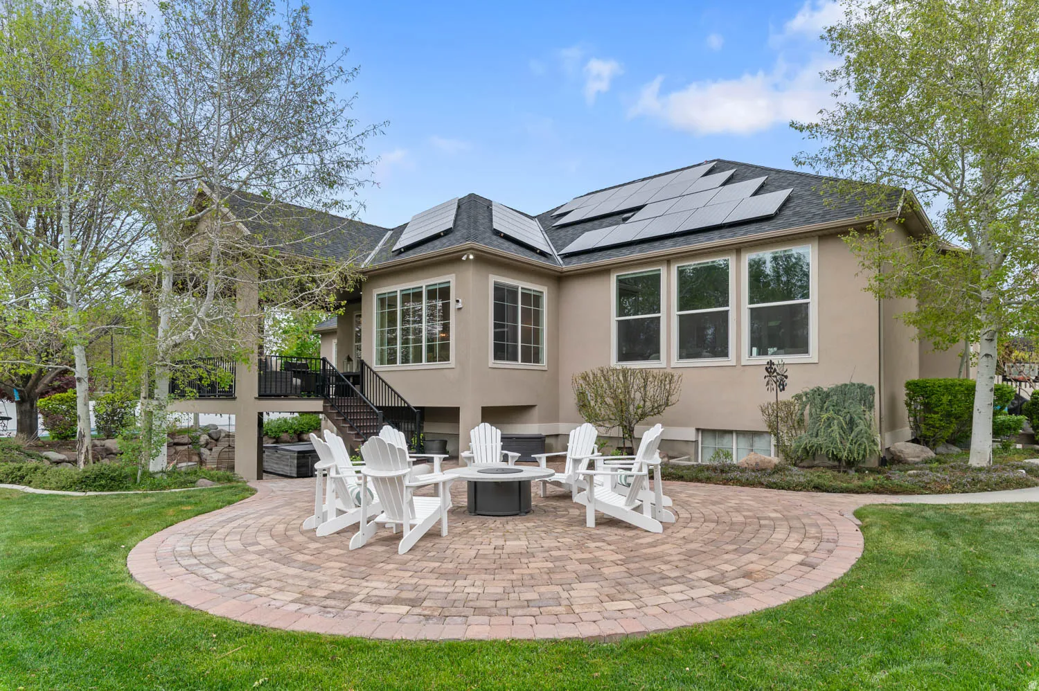 Rear view of house with a patio area, stucco siding, a lawn, and solar panels