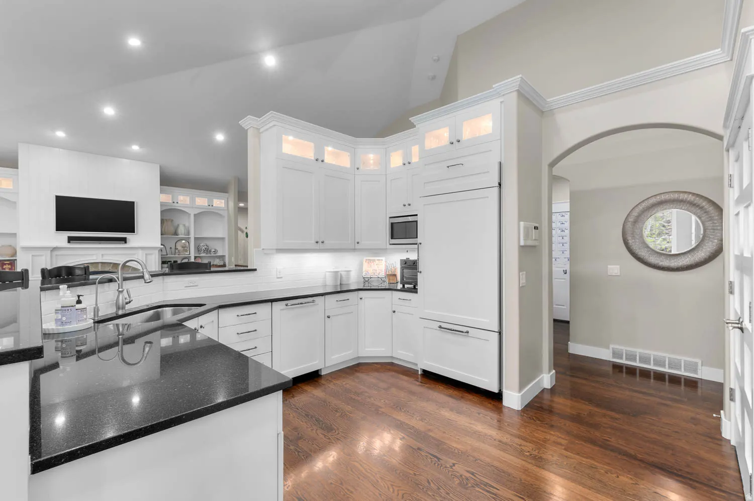 Kitchen featuring arched walkways, dark stone counters, lofted ceiling, white cabinetry, and built in appliances