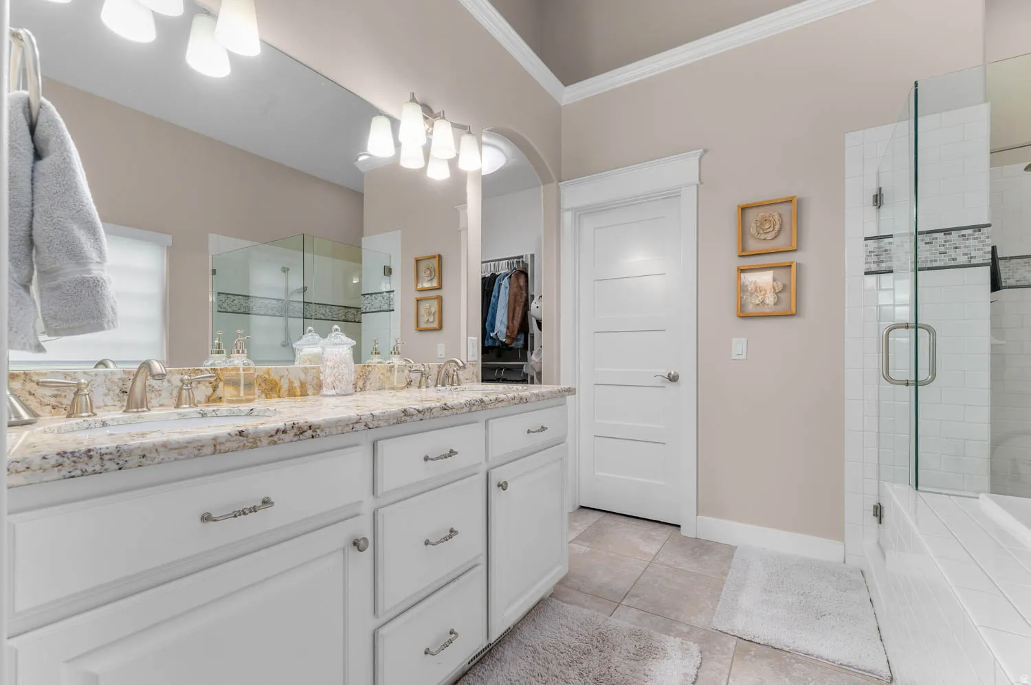 Bathroom with double vanity, a shower stall, a spacious closet, crown molding, and light tile patterned flooring